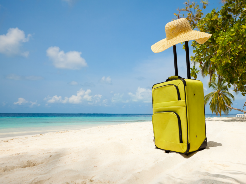 A luggage bag with a hat on it in front of a tropical beach