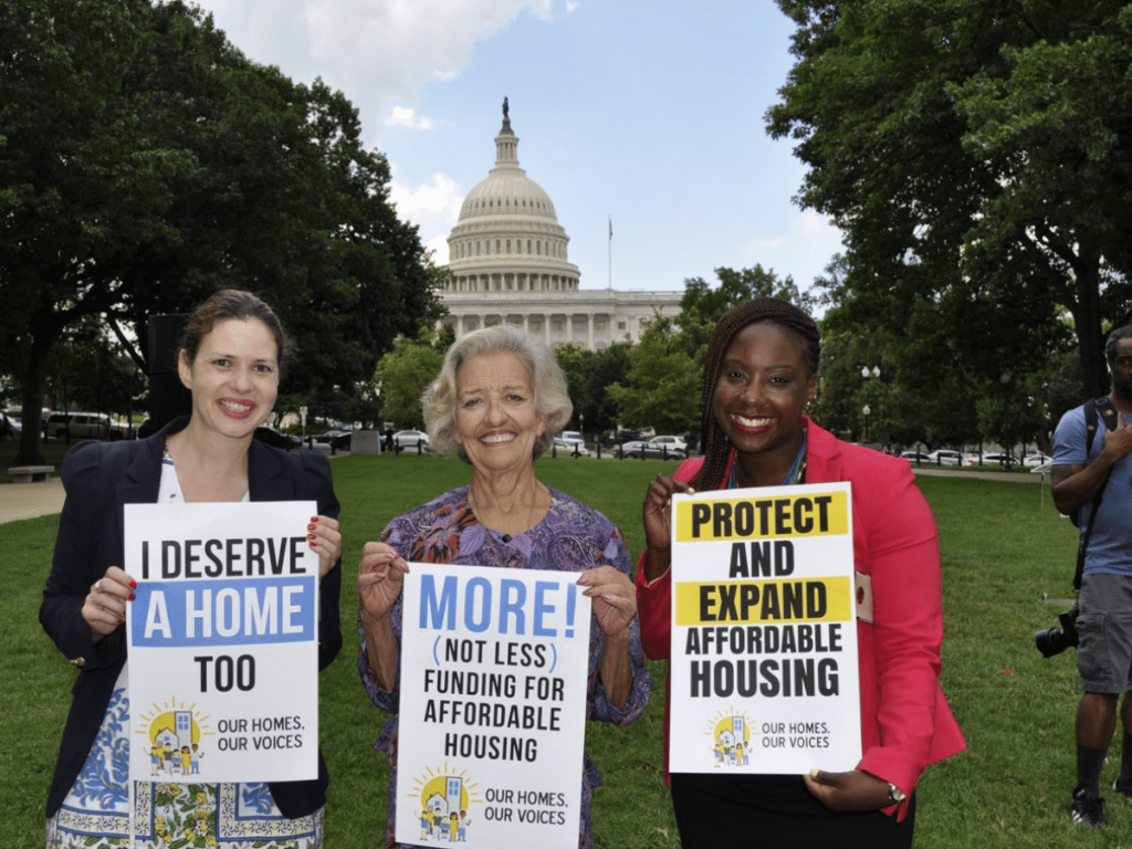 three people in front of the white house holding housing signs