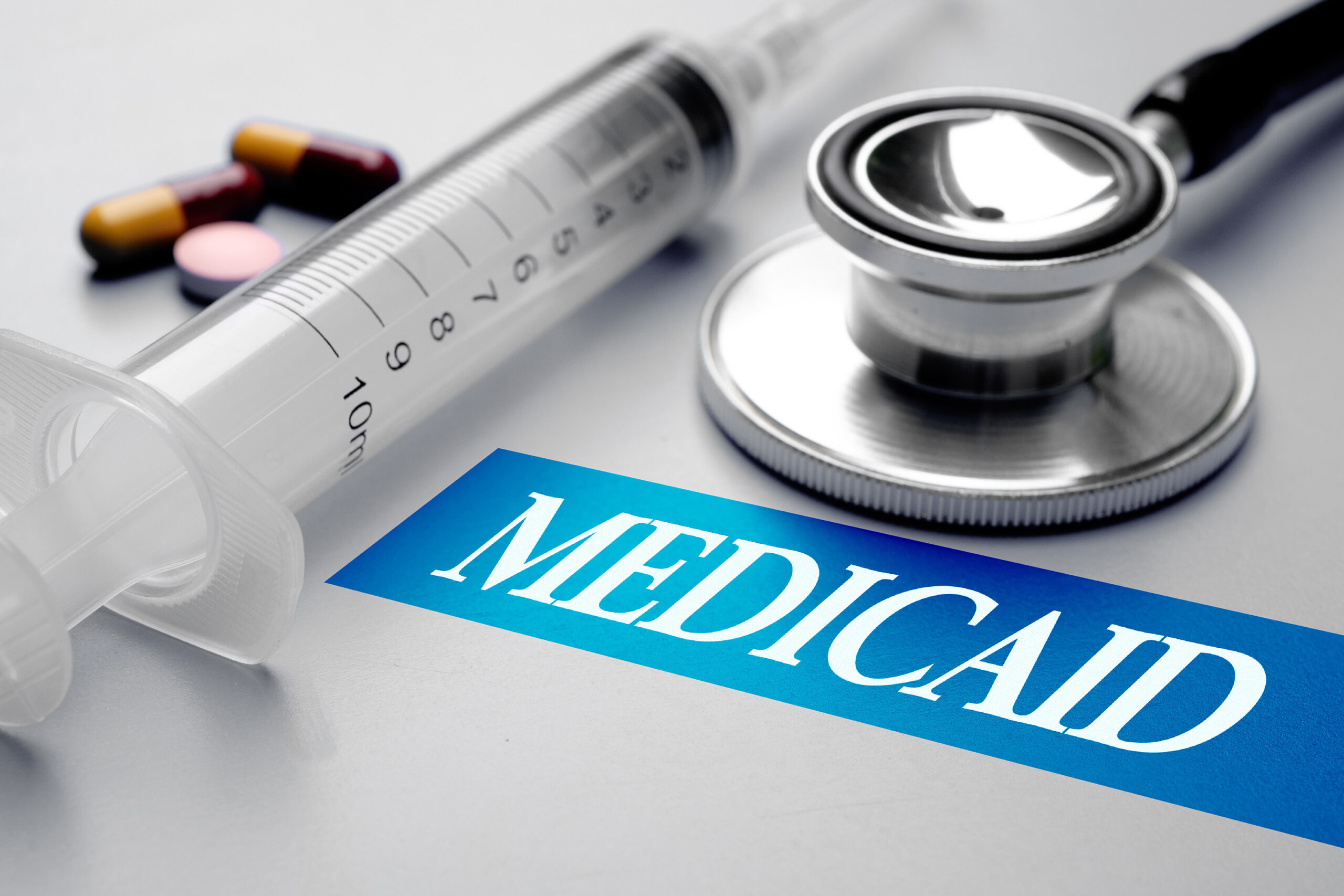 A syringe next to a stethoscope on a table with a label that says medicaid