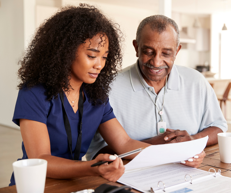 A community health worker dressed in scrubs is sitting with a client looking at paperwork.