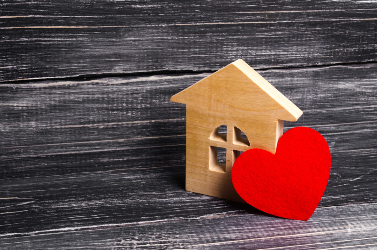 A wooden house block with a red heart, on top of a wooden table. 