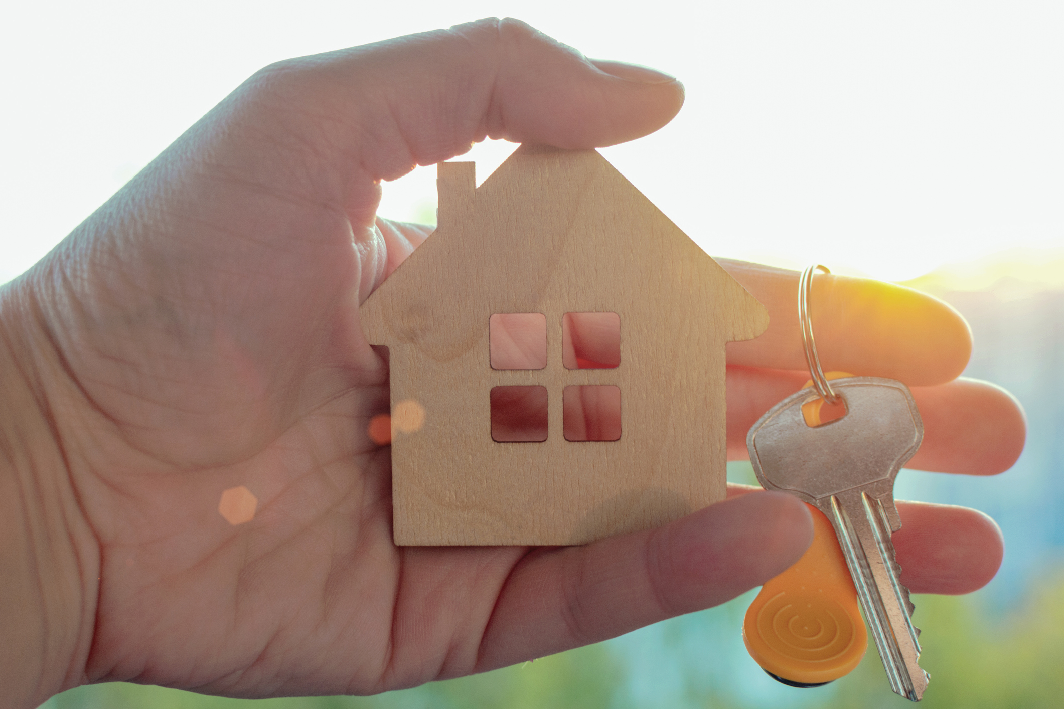 A hand holding a small wooden house keychain