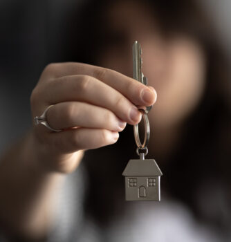 A woman holding up a keychain with a house charm